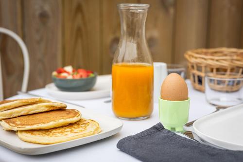 a table with pancakes and an egg and a bottle of orange juice at Chambres d'hôtes Le Studio Bordelais avec bain nordique in Mérignac