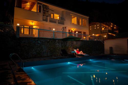 una mujer sentada al lado de una piscina por la noche en MAATI - Signature Collection by Eight Continents, en Nainital