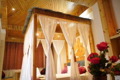 - une chambre avec un lit à baldaquin, des rideaux blancs et des roses dans l'établissement Hotel Gandhi's Paradise, à Dharamshala
