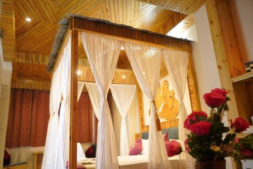 a bedroom with a canopy bed with white curtains and roses at Hotel Gandhi's Paradise in Dharamshala