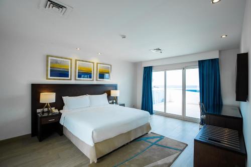 a bedroom with a large white bed and blue curtains at Radisson Blu Resort, Fujairah in Dibba