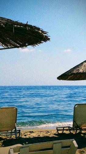 two chairs and umbrellas on a beach with the ocean at Haus Andreas in Néa Meságkala