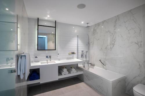 Baño blanco con bañera y lavamanos en Cavo Maris Beach Hotel en Protaras