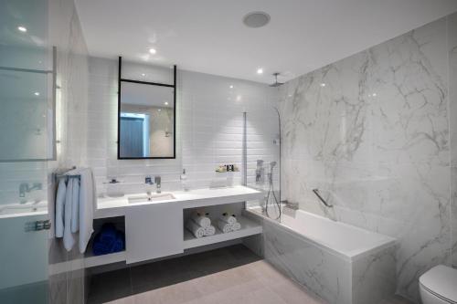 a white bathroom with a tub and a sink at Cavo Maris Beach Hotel in Protaras