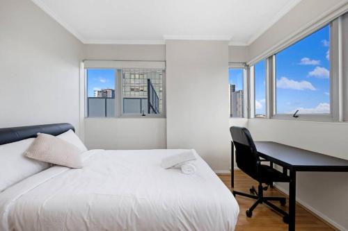 een slaapkamer met een bed, een bureau en ramen bij Sky View 2B1B@burwood in Sydney