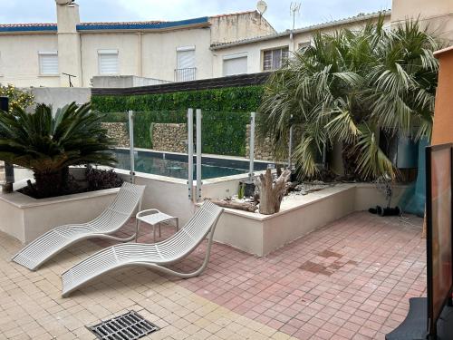 two white benches sitting on a patio with palm trees at Logis Hotel De La Clape in Narbonne-Plage