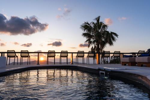 a pool with chairs and a sunset in the background at Mill Houses New Elegant Suites in Firostefani