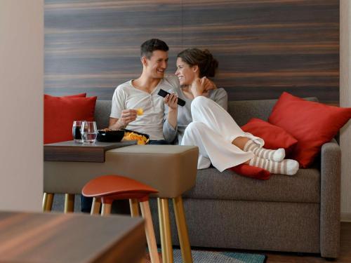 Um homem e uma mulher sentados num sofá a olhar para os telemóveis. em Aparthotel Adagio Bremen City em Bremen