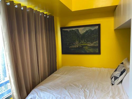 a yellow bedroom with a bed and a painting on the wall at Laugh and Lounge 2 Bedroom Luxury Condo Air residence Makati in Manila