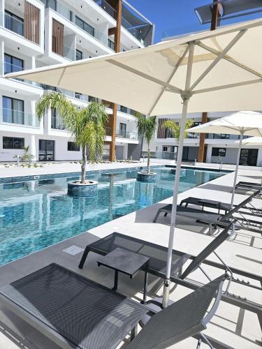 a swimming pool with chairs and an umbrella at New, Modern Studio, Universal Residences in Paphos City