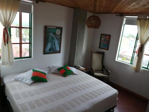 a bedroom with a white bed with green and red pillows at Hotel Veraneras del Quindío in Pueblo Tapao