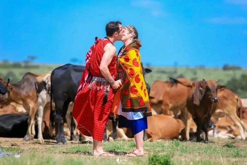 Ein Mann und eine Frau küssen sich vor einer Kuhherde in der Unterkunft NAUNERI HOMES in Sekenani