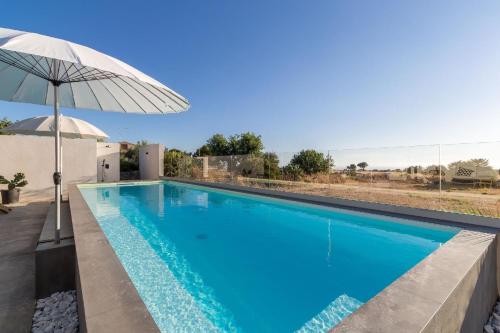a large blue swimming pool with an umbrella at Demetra, moderne Villa mit Pool und Meerblick in Marina di Ragusa