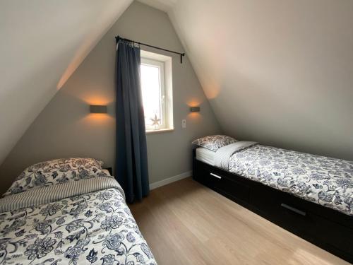 Un dormitorio abuhardillado con dos camas y una ventana. en Vakantiewoning Westkaap, en Westkapelle