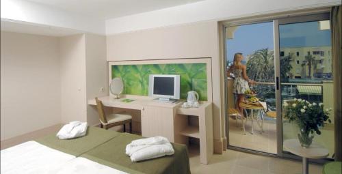 Ambassador Hotel & Spa- All Inclusive في أنطاليا: غرفة نوم مع مكتب مع جهاز كمبيوتر وامرأة على شرفة