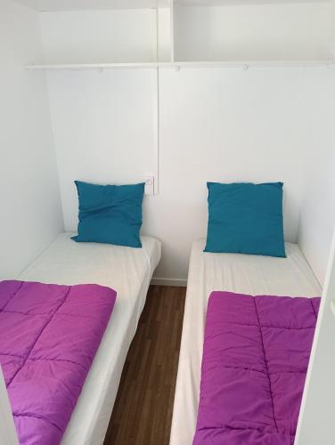 two beds in a room with purple and blue pillows at Camping du Lac in Foix