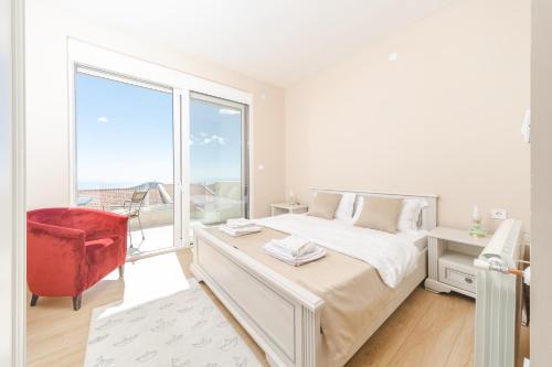 a white bedroom with a large window and a red chair at Villa White Beauty in Lapčići