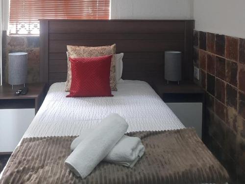 1 dormitorio con cama con sábanas blancas y almohada roja en Cradle Mount Hotel en Krugersdorp