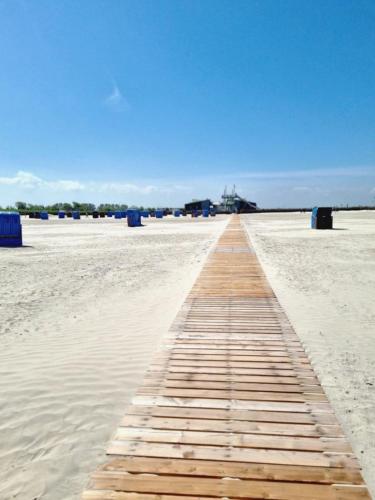 a wooden boardwalk on a beach in the sand at Haus Ankerliebe in Dornum