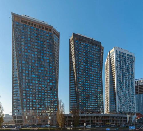 two tall buildings with blue windows in a city at Apartments Center2- Олімпійська - ЖК Manhattan City KПІ -Лесі Українки бульвар in Kyiv