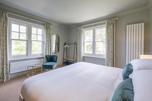 a bedroom with a bed and a chair and windows at Flower Pot Hotel in Henley on Thames