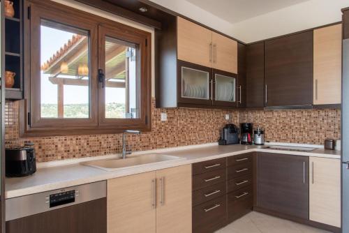 a kitchen with wooden cabinets and a sink and a window at Agnanti Marina villa with private pool in Skouloúfia