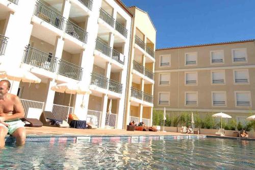 un homme assis dans une piscine à côté d'un bâtiment dans l'établissement Le Mérida, à Juvignac