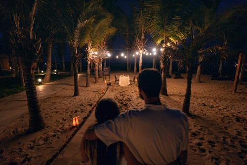 a man holding a baby in front of palm trees at night at Casa Andina Select Zorritos Tumbes in Zorritos
