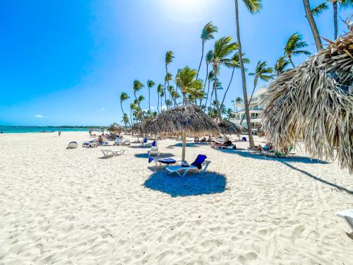 una playa con sillas, palmeras y el océano en DUKASSI SUITES Hotel ROOMS BEACH Bavaro WIFI Parking ROOFTOP POOL & SPA, en Punta Cana