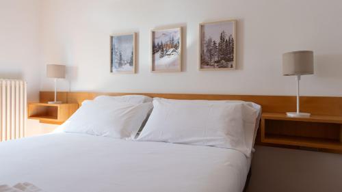 um quarto com uma cama branca com quatro fotografias na parede em San Sebastiano 4 em Bormio
