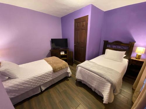 a purple bedroom with two beds and a tv at Hotel Quinta Vista Verde in Antigua Guatemala