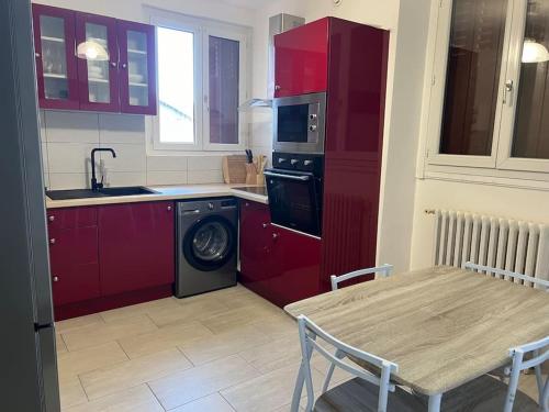 a kitchen with red cabinets and a table and a washing machine at Maison agréable et spacieuse dans le Loiret in Sully-sur-Loire