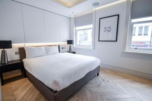 a white bedroom with a bed and a desk and two windows at Cosmopolitan Hideaway in London