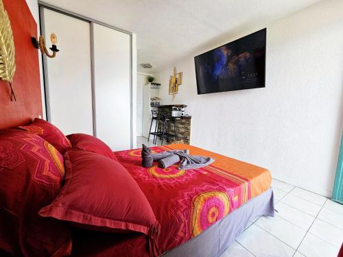 een slaapkamer met een bed met een rode deken en een televisie bij Sweet Crépuscule - Studio avec Vue Mer Imprenable & Piscine in Les Trois-Îlets