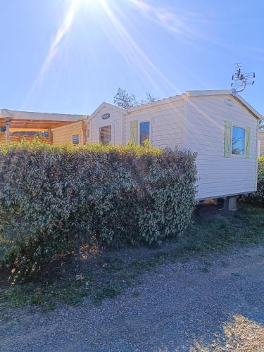 une remorque blanche est garée à côté d'une haie dans l'établissement MOBIL HOME LUCKY climatisé camping NOVELA PORT LA NOUVELLE, à Port-la-Nouvelle
