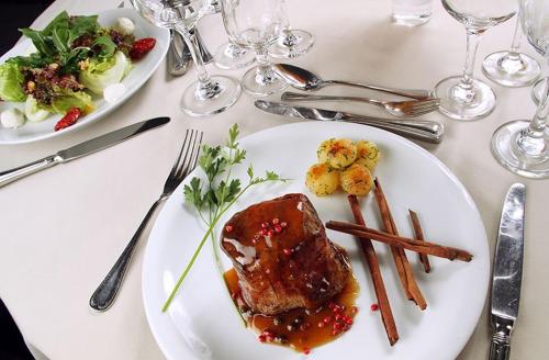 a white plate with meat and vegetables on a table at Rafain Palace Hotel & Convention Center in Foz do Iguaçu