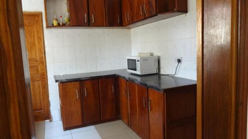 a kitchen with wooden cabinets and a microwave on a counter at Londoninnn in Bijilo