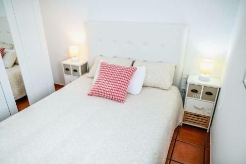 a white bed with a red checked pillow on it at Acogedora casita in El Charco