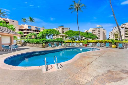 a swimming pool at a resort with chairs and palm trees at Kahana Villa in Lahaina