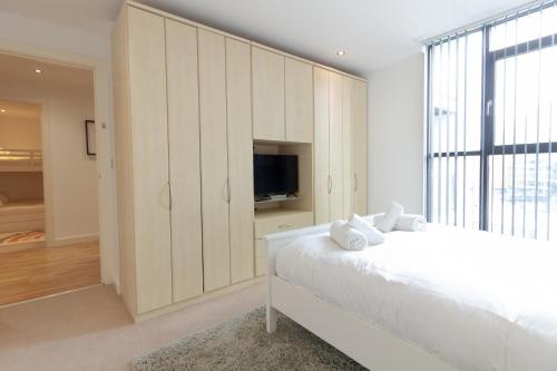 a white bedroom with a large bed and a tv at Central Gem: Cosy 2BR with Private Balcony in Manchester