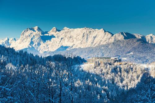 a snow covered mountain range with a building in the foreground w obiekcie Kempinski Hotel Berchtesgaden w mieście Berchtesgaden