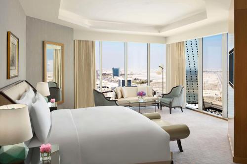 a bedroom with a large white bed and a living room at Kempinski Al Othman Hotel Al Khobar in Al Khobar