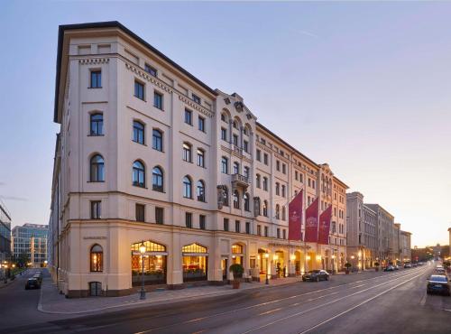 a large white building on a city street with cars parked at Vier Jahreszeiten Kempinski München in Munich