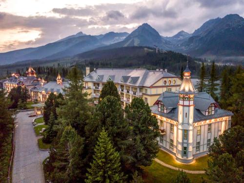 a large building with a clock tower in front of mountains at Grand Hotel Kempinski High Tatras in Štrbské Pleso
