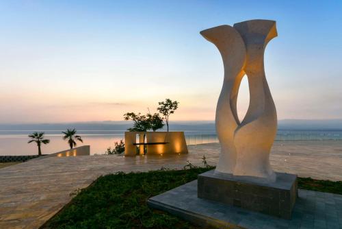 uma estátua em frente ao oceano ao pôr do sol em Kempinski Hotel Ishtar Dead Sea em Sowayma