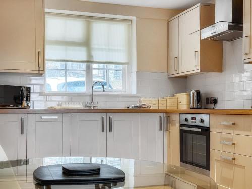 a kitchen with white cabinets and a black stool at Castleriggs Cottage - Uk45178 in Threlkeld