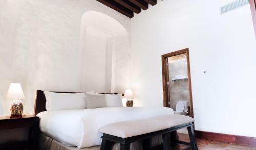 a white bedroom with a large bed and a stool at Quinta Real Oaxaca in Oaxaca City