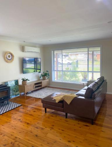 a living room with a couch and a large window at OAK FLATS - Cosy Getaway in Lake Illawarra
