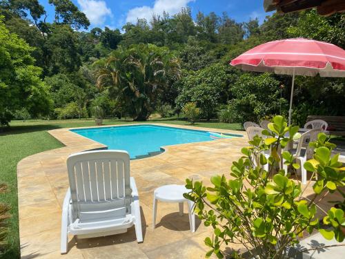 a group of chairs and an umbrella next to a swimming pool at Recanto da Floresta - Casa de campo em Secretário in Petrópolis
