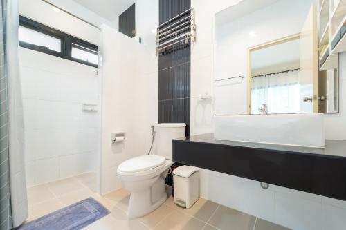 La salle de bains blanche est pourvue de toilettes et d'un miroir. dans l'établissement Baan Promphan Premium, à Phuket